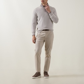 Model wearing Eleventy sand cotton trousers with a light grey half-zip knit and brown suede trainers.