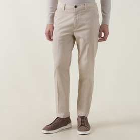 Model wearing Eleventy sand cotton trousers with slim fit, styled with brown suede slip-on shoes and a light grey knit top.