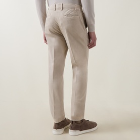 Model wearing Eleventy sand cotton-elastane trousers, rear view, styled with brown suede trainers.