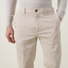 Model wearing Eleventy sand cotton chino trousers, styled with a cream knit jumper, close-up of waist and leg detail.