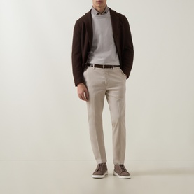 Model wearing Eleventy sand cotton trousers, styled with a dark brown cardigan, grey sweatshirt, and brown trainers.