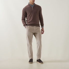 Model wearing Eleventy sand cotton trousers styled with a brown quarter-zip knit, blue shirt, and dark trainers.