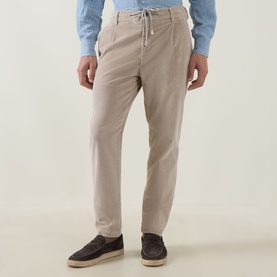 Model wearing Eleventy sand cotton trousers with elasticated drawstring waist, styled with a blue shirt and dark espadrilles.
