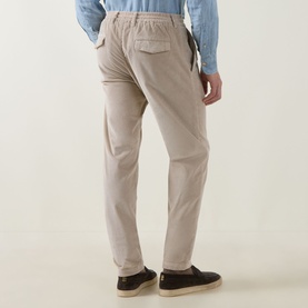 Model wearing Eleventy sand cotton trousers, rear view, shown with a chambray shirt and dark navy loafers.