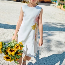 Model wearing Patachou watercolour print dress with floral detail, sleeveless tiered hem design, styled with gold earrings, holding sunflowers