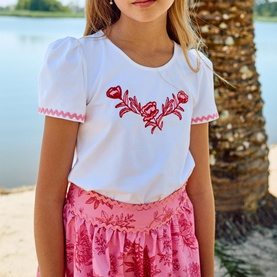 Model wearing Patachou white T-shirt with red floral embroidery and pink ric-rac trim, styled with a pink floral skirt.