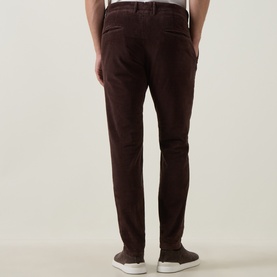 Model wearing Slowear brown casual trousers in cotton-elastane, shown from behind with white trainers visible.