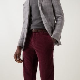 Model wearing Slowear burgundy casual corduroy trousers, styled with a grey check blazer and brown leather belt.