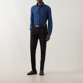 Model wearing blue long-sleeve shirt tucked into slim black trousers, styled with a brown leather belt and dark loafers