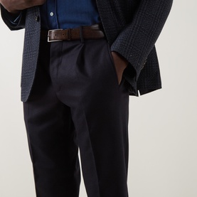 Model wearing navy tailored trousers with centre pleat, styled with a navy check blazer, blue shirt, and brown leather belt