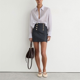 Model wearing Reiss dark blue mini skirt with gold double-breasted buttons, styled with white blouse, cream flats, and brown handbag.