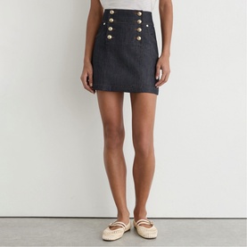 Model wearing Reiss dark blue mini skirt with gold button detail, styled with white Mary Jane flats and a white top.
