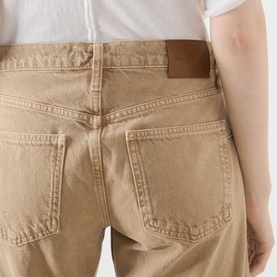 Model wearing Free People Oat Latte jeans, close-up of back pockets showing tan denim and brown leather patch detail