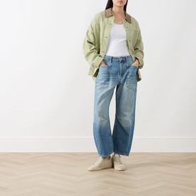 Model wearing Free People Minimalist Moxi Barrel-Leg Jeans in County Fair mid-wash blue, styled with sage green jacket and white tee.