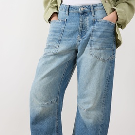 Model wearing Free People Minimalist Moxi Barrel-Leg Jeans in County Fair, low-rise barrel-leg with front patch pockets, styled with olive jacket