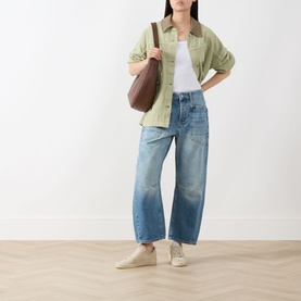 Model wearing Free People Minimalist Moxi Barrel-Leg Jeans in County Fair mid-wash denim, styled with sage shirt and white trainers.