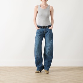 Model wearing Free People blue wide-leg jeans in mid-wash denim with a grey ribbed tank top and tan shoes