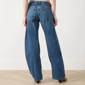 Model wearing Free People blue wide-leg jeans, rear view, brown leather patch waistband detail, relaxed fit, 100% cotton denim