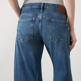 Model wearing Free People blue wide-leg jeans in 100% cotton denim, close-up rear view showing back pockets and waistband detail.
