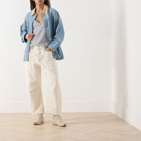 Model wearing Free People We The Free Minimalist Moxie Low-Rise Barrel Jeans in Dusty Roads, styled with a denim shirt and grey tee