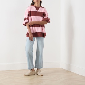 Model wearing Free People V-Insert Striped Sweater in Strawberry Wine Comb, pink and burgundy stripes, with light blue wide-leg jeans and white