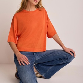 Model wearing Mint Velvet orange boxy cropped t-shirt with short sleeves, styled with blue wide-leg jeans