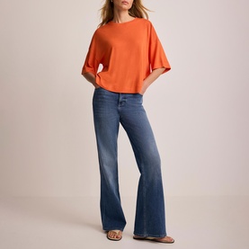 Model wearing Mint Velvet orange oversized short-sleeve top with wide sleeves, styled with blue flared jeans and strappy sandals
