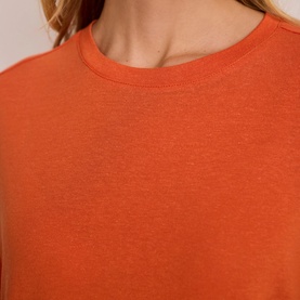 Model wearing Mint Velvet orange crew neck top, close-up of neckline and fabric detail.