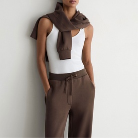 Model wearing Reiss mocha brown jogger trousers with tie waist, styled with white sleeveless top and matching brown scarf tied at neck