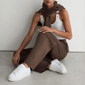 Model wearing Reiss mocha brown dungarees with white vest top, styled with white leather trainers and brown scarf