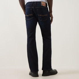 Model wearing Diesel 2007 Zatiny Bootcut Jeans in dark blue with tobacco stitching and logo patch detail, rear view.