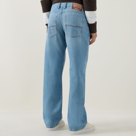Model wearing Diesel 3049 loose jeans in light blue, rear view, styled with a brown cropped jacket and white trainers.