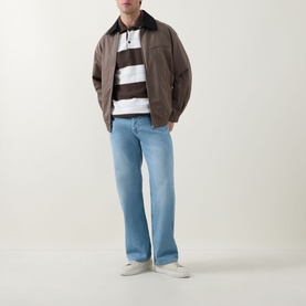 Model wearing Diesel 3049 loose light blue jeans with brown jacket and brown striped rugby polo, styled with white trainers