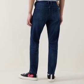 Model wearing Diesel 3049 dark blue skinny jeans, rear view, styled with black canvas low-top trainers with red logo detail.