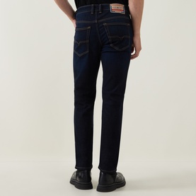 Model wearing Diesel 3049 slim jeans in dark blue, rear view, with orange branded patch detail and black leather shoes.