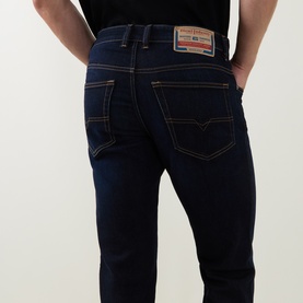 Model wearing Diesel 3049 dark blue slim jeans, rear view showing contrast orange stitching and branded leather patch detail.