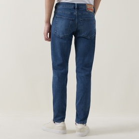Model wearing Diesel 3049 slim jeans in mid blue, rear view, with white trainers visible at hem.