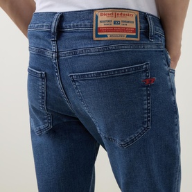 Model wearing Diesel 3049 slim jeans in mid blue, rear view showing branded patch, red tab detail and back pockets.