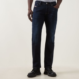 Model wearing Diesel 1985 Larkee Straight Leg Jeans in dark blue with whiskering and faded details, styled with black leather boots.