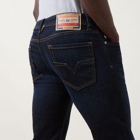 Model wearing Diesel 1985 Larkee Straight Leg Jeans in dark blue with tobacco stitching, logo badge, and five-pocket styling.