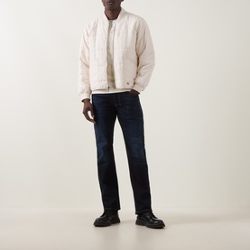 Model wearing Diesel 1985 Larkee Straight Leg Jeans in dark blue with whiskering details, styled with a cream quilted bomber jacket and black boots.