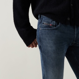 Model wearing Diesel 3049 straight jeans in dark blue denim, close-up of back pocket with branded logo patch, styled with black knit top.