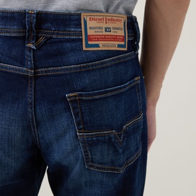 Model wearing Diesel 3049 Tapered Jeans in dark blue, close-up of back pocket with branded logo patch and contrast stitching detail.