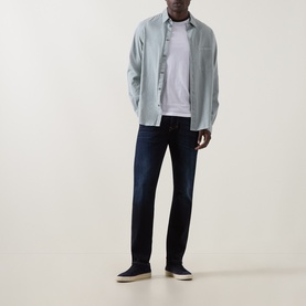 Model wearing Diesel 1986 Larke-Beex Tapered Jeans in dark blue, styled with a light blue overshirt, white tee and navy slip-on shoes.