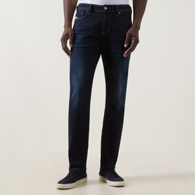 Model wearing Diesel 1986 Larke-Beex Tapered Jeans in dark blue with tobacco stitching and dark wash finish, styled with white trainers.