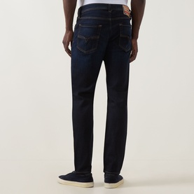 Model wearing Diesel 1986 Larke-Beex Tapered Jeans in dark blue, rear view showing five-pocket design and tobacco stitching, styled with white
