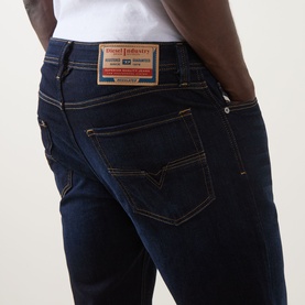 Model wearing Diesel 1986 Larke-Beex Tapered Jeans in dark blue with tobacco stitching and branded patch detail, paired with a white tee.
