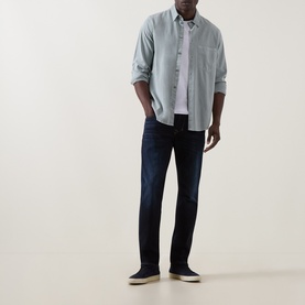Model wearing Diesel 1986 Larke-Beex Tapered Jeans in dark blue, styled with a light blue shirt and navy canvas shoes.