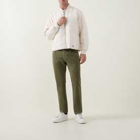 Model wearing Diesel 1986 Larke-Beex Tapered Jeans in green khaki wash, styled with a cream bomber jacket and white trainers.
