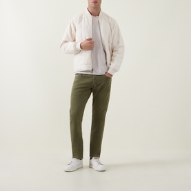 Model wearing Diesel 1986 Larke-Beex Tapered Jeans in green khaki wash, styled with a cream bomber jacket and white trainers.